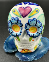 Load image into Gallery viewer, Inspired by nature, this ceramic skull statuette is full of vibrant color and intricate details that I hand painted. The primary color is white with multi-color floral motifs that are painted across the skull, along with hearts and leaves and lively colorful accents around the entire skull. 
