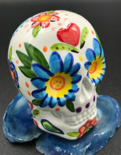 Load image into Gallery viewer, Inspired by nature, this ceramic skull statuette is full of vibrant color and intricate details. The primary color is white with Multi-color floral motifs that are painted across the skull, along with hearts and leaves and lively colorful accents around the entire skull. 
