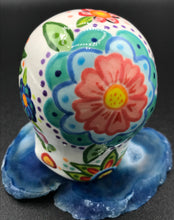Load image into Gallery viewer, Inspired by nature, this ceramic skull statuette is full of vibrant color and intricate details. The primary color is white with Multi-color floral motifs that are painted across the skull, along with hearts and leaves and lively colorful accents around the entire skull.
