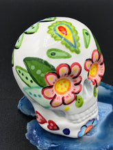 Load image into Gallery viewer, Inspired by nature, this ceramic skull statuette is full of vibrant color and intricate details that I hand painted. The primary color is white with multi-color floral motifs that are painted across the skull, along with hearts and leaves and lively colorful accents around the entire skull. 
