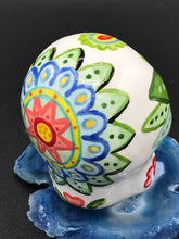 Load image into Gallery viewer, Inspired by nature, this ceramic skull statuette is full of vibrant color and intricate details that I hand painted. The primary color is white with multi-color floral motifs that are painted across the skull, along with hearts and leaves and lively colorful accents around the entire skull. 
