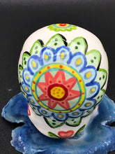 Load image into Gallery viewer, Inspired by nature, this ceramic skull statuette is full of vibrant color and intricate details that I hand painted. The primary color is white with multi-color floral motifs that are painted across the skull, along with hearts and leaves and lively colorful accents around the entire skull. 
