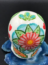 Load image into Gallery viewer, Inspired by nature, this ceramic skull statuette is full of vibrant color and intricate details. The primary color is white with multi-color floral motifs that are painted across the 
