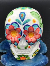 Load image into Gallery viewer, Inspired by nature, this ceramic skull statuette is full of vibrant color and intricate details. The primary color is white with multi-color floral motifs that are painted across the 
