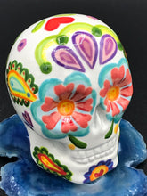 Load image into Gallery viewer, Inspired by nature, this ceramic skull statuette is full of vibrant color and intricate details that I hand painted. The primary color is white with multi-color floral motifs that are painted across the skull, along with hearts and leaves and lively colorful accents around the entire skull. 
