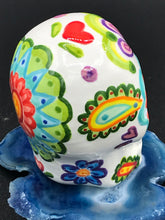 Load image into Gallery viewer, Inspired by nature, this ceramic skull statuette is full of vibrant color and intricate details that I hand painted. The primary color is white with multi-color floral motifs that are painted across the skull, along with hearts and leaves and lively colorful accents around the entire skull. 
