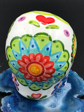 Load image into Gallery viewer, Inspired by nature, this ceramic skull statuette is full of vibrant color and intricate details that I hand painted. The primary color is white with multi-color floral motifs that are painted across the skull, along with hearts and leaves and lively colorful accents around the entire skull. 
