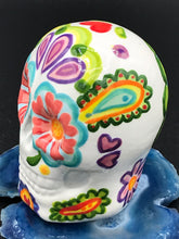 Load image into Gallery viewer, Inspired by nature, this ceramic skull statuette is full of vibrant color and intricate details that I hand painted. The primary color is white with multi-color floral motifs that are painted across the skull, along with hearts and leaves and lively colorful accents around the entire skull. 

