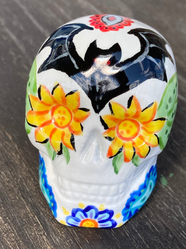 This Ceramic Skull Art With Bat Silhouettes And Flowers is a beautiful mini goth witchy altar skull, with detailed hand painted features. Inspired by the vibrant blooms of the Dawn Redwood, it captures the beauty of the changing of seasons. Perfect for adding a touch of whimsical enchantment to any home. Measurements: H 2 3/4” x W 2” x D 2”