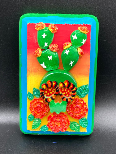 This handcrafted polymer clay wall art features a wood frame painted in a gradient from light yellow to dark red, creating a stunning sunset look. With a bright green skull cactus plant and bright yellow blooming flowers. Boasting vivid marigold blooms and a bright teal and green hue frame to make a bold contrast with the warm background hue. this piece is sure to make a statement.  Measurements: