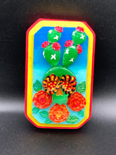 Load image into Gallery viewer, This handcrafted polymer clay wall art features a wood frame painted in a gradient from light to dark blue, creating a stunning starry night sky look. With a bright green skull cactus plant and bright yellow blooming flowers. Boasting vivid marigold blooms and a bright yellow and red hue frame to make a bold contrast with the warm background hue. This piece is sure to make a statement.
