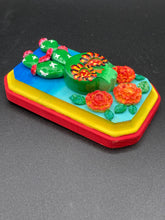 Load image into Gallery viewer, This handcrafted polymer clay wall art features a wood frame painted in a gradient from light to dark blue, creating a stunning starry night sky look. With a bright green skull cactus plant and bright yellow blooming flowers. Boasting vivid marigold blooms and a bright yellow and red hue frame to make a bold contrast with the warm background hue. This piece is sure to make a statement.
