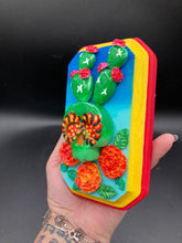 Load image into Gallery viewer, This handcrafted polymer clay wall art features a wood frame painted in a gradient from light to dark blue, creating a stunning starry night sky look. With a bright green skull cactus plant and bright yellow blooming flowers. Boasting vivid marigold blooms and a bright yellow and red hue frame to make a bold contrast with the warm background hue. This piece is sure to make a statement.
