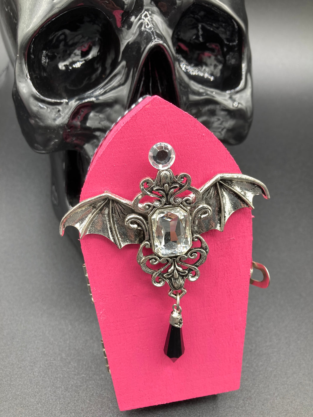 This unique handmade Pink Spooky Glam Wood Coffin Ring Box offers a statement piece for your witchy home decor. Its macabre collections boast a black and pink wood coffin with large shimmery bat embellishments and decorative black crystals around the exterior. Open up the box to find a bright turquoise mandala fabric and a tiny black crystal bat decoration for a truly eerie feel.