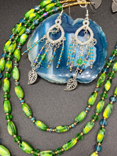 Load image into Gallery viewer, These large chandelier-style earrings feature blues, greens, and iridescent glass beads as well as a finely crafted silver plated leaf charm for added detail. Perfect for bohemian-inspired looks, these versatile earrings can elevate any wardrobe from whimsical hippie to boho chic.  Measurements: 3 1/4” in length
