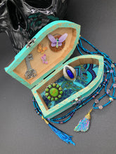 Load image into Gallery viewer, This Whimsical Fairy Wood Coffin Box is a truly unique and magical piece of home decor. With its vibrant turquoise exterior and eye-catching mini door knob, this Steampunk-inspired box is sure to be a conversation starter. Inside, the glittery gold interior and colorful butterfly detailing will bring a touch of fantasy to any room. The silver key and accompanying iridescent crystals complete the mystical and pastel goth look!
