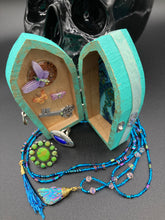 Load image into Gallery viewer, This Whimsical Fairy Wood Coffin Box is a truly unique and magical piece of home decor. With its vibrant turquoise exterior and eye-catching mini door knob, this Steampunk-inspired box is sure to be a conversation starter. Inside, the glittery gold interior and colorful butterfly detailing will bring a touch of fantasy to any room. The silver key and accompanying iridescent crystals complete the mystical and pastel goth look!
