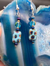Load image into Gallery viewer, This set of glass beaded earrings features a vibrant blue shade with hints of purples and gold for an overall dynamic look. Its unique texture is derived from the combination of different size and shaped beads, resulting in a bold, eye-catching piece. For any discerning connoisseur, this set is a must-have addition to any jewelry collection.  Measurements: 1 1/2” in length
