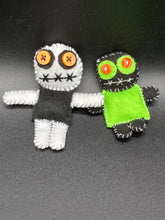 Load image into Gallery viewer, Black and white Voodoo Doll stand at 3 3/4&quot; in height.  He has a black torso with white arms and legs, and a big round white head.  Bulging yellow/orange buttons for eye and his mouth is sowed shut but despite that he kinda looks like he’s smiling.  Tiny black and lime green Voodoo Doll stands at 3&quot; in height. He has a lime green torso but the rest is black.  He has a tiny round head with tiny orange buttons for eyes which makes him look cute.  His mouth is sowed shut of course.
