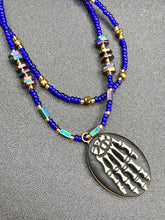 Load image into Gallery viewer, This spooky resin anatomical skeleton hand pendant is a perfect handy jewelry piece! The anatomical skeleton hand is made of resin with brass metal backing. Rich royal blue glass beads to give it a huge pop of color. Rectangular and hexagon rainbow hematite beads to compliment the shapes of the finger bones in the pendant. Bright canary yellow beads along the strands to break up the cool hues a bit. Necklace measures 16” adjustable up to 18” in length, pendant is 1 1/4”
