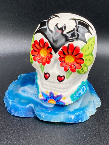 This mini ceramic sugar skull is an intricate piece of art, inspired by nature and drenched in vibrant colors and details. Featuring a white base and multi-colored floral motifs, notable features include hearts and leaves as well as lively accents that encircle the skull. A beautiful Dia De Los Muertos or Day of the Dead-themed decoration.  Measurements: H 2 3/4” x W 2” x D 2”