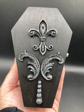 Load image into Gallery viewer, This vintage-inspired coffin ring box will make a spooky yet cute addition to any jewelry collection. The sleek black box has eye-catching black and gray embellishments, while the interior is beautifully decorated with a vivid turquoise blue fabric and a highly detailed black and silver cross with dark red roses. Function and style meet with this unique and stylish piece.

