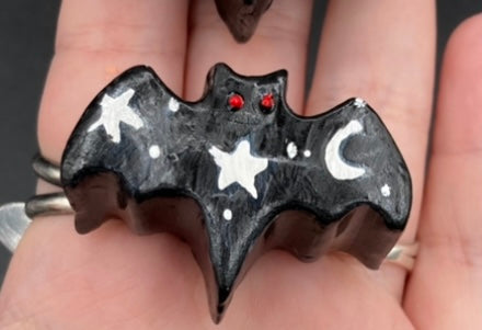 Cute and spooky magnet design to adorn your refrigerator, lockers, workstation, toolbox, or dishwasher. This hand-sculpted clay bat statuette all black with white stars to recreate a starry night sky. H 1” x W 2” x D 1/2”
