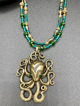 Load image into Gallery viewer, This Steampunk Brass Octopus Emerald Eyes Choker Style Necklace is an eye-catching piece for cosplay and gothic aficionados alike. Crafted with a large brass octopus pendant, emerald green eyes, and an adjustable glass beaded strand, this necklace is sure to turn heads. Featuring a range of light and dark green, gold, and brass tones, this necklace complements any sci-fi, fantasy, or steampunk ensemble.  Measurements: 15 1/2” adjustable up to 17" in length
