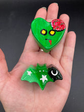 Load image into Gallery viewer, Perfect cute and spooky Halloween item to add to your fridge, locker, cubicle or toolbox. This handcrafted, bright green, heart-shaped magnet features an intricate, exposed brains-inspired zombie design. This hand-sculpted clay bat statuette boasts stunning ombre coloration, transitioning from black to dark green to light green to recreate the breathtaking look of a starry night sky.
