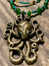 Load image into Gallery viewer, This Steampunk Brass Octopus Emerald Eyes Choker Style Necklace is an eye-catching piece for cosplay and gothic aficionados alike. Crafted with a large brass octopus pendant, emerald green eyes, and an adjustable glass beaded strand, this necklace is sure to turn heads. Featuring a range of light and dark green, gold, and brass tones, this necklace complements any sci-fi, fantasy, or steampunk ensemble.  Measurements: 15 1/2” adjustable up to 17" in length
