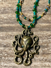 Load image into Gallery viewer, This Steampunk Brass Octopus Emerald Eyes Choker Style Necklace is an eye-catching piece for cosplay and gothic aficionados alike. Crafted with a large brass octopus pendant, emerald green eyes, and an adjustable glass beaded strand, this necklace is sure to turn heads. Featuring a range of light and dark green, gold, and brass tones, this necklace complements any sci-fi, fantasy, or steampunk ensemble.  Measurements: 15 1/2” adjustable up to 17" in length
