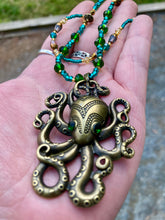 Load image into Gallery viewer, This Steampunk Brass Octopus Emerald Eyes Choker Style Necklace is an eye-catching piece for cosplay and gothic aficionados alike. Crafted with a large brass octopus pendant, emerald green eyes, and an adjustable glass beaded strand, this necklace is sure to turn heads. Featuring a range of light and dark green, gold, and brass tones, this necklace complements any sci-fi, fantasy, or steampunk ensemble.  Measurements: 15 1/2” adjustable up to 17" in length
