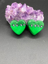 Load image into Gallery viewer, Perfect cute and spooky Halloween item to add to your fridge, locker, cubicle or toolbox. This hand-crafted light and dark green heart-shaped magnet showcases a Frankenstein-inspired design.  Measurements: H 1 1/2” x W 1 5/8” x D 1/2”
