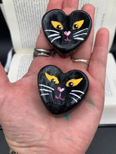 Load image into Gallery viewer, Perfect cute and spooky Halloween magnet art to add to your fridge, locker, cubicle or toolbox.  This hand-crafted heart-shaped magnet features a figurine of a black cat with distinctive yellow eyes. Measurements: H 1 1/2” x W 1 5/8” x D 1/2”
