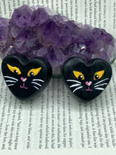 Load image into Gallery viewer, Perfect cute and spooky Halloween magnet art to add to your fridge, locker, cubicle or toolbox.  This hand-crafted heart-shaped magnet features a figurine of a black cat with distinctive yellow eyes. Measurements: H 1 1/2” x W 1 5/8” x D 1/2”

