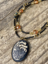 Load image into Gallery viewer, This spooky resin anatomical heart pendant is too cute!!! The pendant is made of resin with brass metal backing. An assortment of floral metal beads to give it a contrast to the soft, dainty style of the glass beaded necklace. Tiny shimmer black glass beads with yellow and orange glass beads to give it a pop of color.  Necklace measures 16” adjustable up to 18” in length, pendant is 1 1/4” Height
