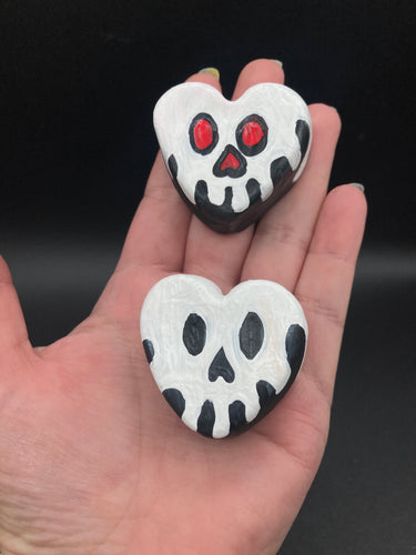 Perfect cute and spooky Halloween magnet art to add to your fridge, locker, cubicle or toolbox.  This hand-crafted black heart-shaped magnet features a white skull figurine  with distinctive red and black eyes.   Measurements: H 1 1/2” x W 1 5/8” x D 1/2”