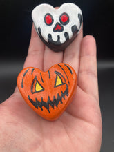 Load image into Gallery viewer, Perfect cute and spooky Halloween magnet art to add to your fridge, locker, cubicle or toolbox.  This hand-crafted black heart-shaped magnet features a white skull figurine  with distinctive red eyes. Heart-shaped bright orange Jack O Lantern theme magnet.  Measurements: H 1 1/2” x W 1 5/8” x D 1/2”
