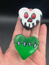 Load image into Gallery viewer, Perfect cute and spooky Halloween magnet art to add to your fridge, locker, cubicle or toolbox.  This hand-crafted black heart-shaped magnet features a white skull figurine  with distinctive red eyes. Heart-shaped green Frankenstein theme magnet.  Measurements: H 1 1/2” x W 1 5/8” x D 1/2”
