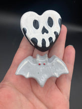 Load image into Gallery viewer, Perfect cute and spooky Halloween magnet art to add to your fridge, locker, cubicle or toolbox.  This hand-crafted black heart-shaped magnet features a white skull figurine  with distinctive black eyes. Cute all light gray bat with white highlights with red eyes magnet.
