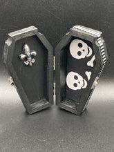 Load image into Gallery viewer, This unique vintage-inspired ring box is perfect for storing your jewelry and other special items. The wood coffin design is accented with a detailed floral black silver cross and a white and black ribbon. The interior is lined with a skull fabric and a fleur de lis embellishment, adding a spooky yet cute flair.
