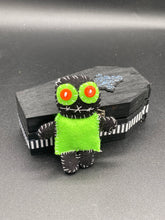 Load image into Gallery viewer, Lime green and black voodoo doll stands at 3&quot; in height. He has a lime green torso but the rest is black. He has a tiny round head with tiny orange buttons for eyes which makes him look cute. His mouth is sowed shut of course so good luck trying to talk to him.
