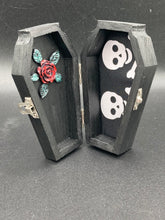 Load image into Gallery viewer, This unique vintage-inspired ring box is perfect for storing your jewelry and other special items. The wood coffin design is accented with a detailed black silver cross. The interior is lined with a skull fabric and a large dark red rose, adding a spooky yet elegant flair.
