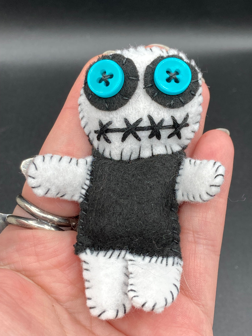 Black and white Voodoo Doll has a black torso, white arms and legs and both round white head with bulging large turquoise buttons, he’s just funny looking. 3 1/2