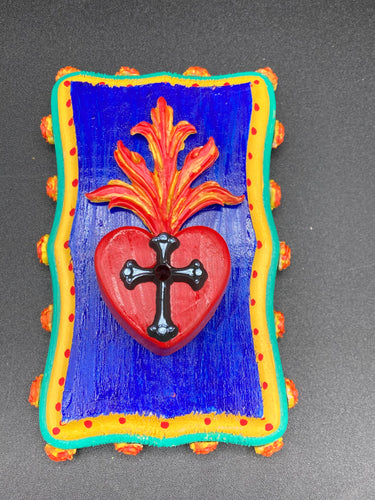 This Sacred Heart Wall Art Decor is the perfect way to enhance your home with an artistic flair. This Sacred Heart Wall Art Decor is crafted with a stunning red heart detailed with a black-silver cross and a vibrant fire embellishment at its center. Adding to its unique traditional Mexican aesthetic, the wood frame is decorated with marigold flowers, creating a beautiful and eye-catching artwork.