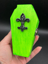 Load image into Gallery viewer, This Lime Green BeetleJuice-inspired Wood Coffin Ring Box is perfect for storing special items. The eye-catching black-silver fleur de lis embellishment and the black and white stripped ribbon gives the box a unique and spooky, yet cute and misfit look. Its all-black interior elevates the aesthetic of this stylish box.
