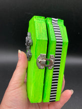 Load image into Gallery viewer, This Lime Green BeetleJuice-inspired Wood Coffin Ring Box is perfect for storing special items. The eye-catching black-silver fleur de lis embellishment and the black and white stripped ribbon gives the box a unique and spooky, yet cute and misfit look. Its all-black interior elevates the aesthetic of this stylish box.
