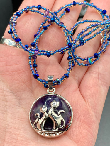 This stylish necklace features a shimmery sterling silver amethys pendant with cats and stars, making it the perfect accessory for any cat lover. With two-hole blue beads compliments the dark dark purple hues glass beads, this double strand necklace holds a round kitty pendant made with various hues of purple, blue and gold tone glass beads. Add a touch of purrfection to your look with this statement piece.   Measurements:  Necklace is 15 1/2” adjustable up to 18