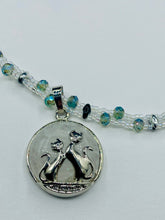 Load image into Gallery viewer, This stylish necklace features a shimmery sterling silver quartz pendant with cats and stars, making it the perfect accessory for any cat lover. With two-hole silver and black beads that stand out against the light aquamarine glass beads, this double strand necklace holds a round kitty pendant made with various hues of clear and iridescent glass beads. Add a touch of purrfection to your look with this statement piece.  Measurements:  Necklace is 15”adjustable up to 18&quot; 
