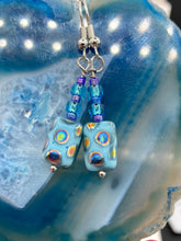 Load image into Gallery viewer, Glass beaded earrings take center stage in this design, with light blue glass beads as the primary color. These beads contain varying shades of blue, purple, and a hint of gold to add interest and texture to the style. As a show-stopping accessory, this piece of jewelry is a must-have for any collection.  Measurements: 1 3/8” in length
